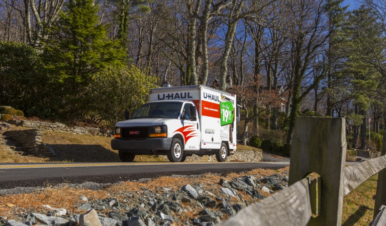 A U-Haul Rental Truck travelling down a road next to a wooded area