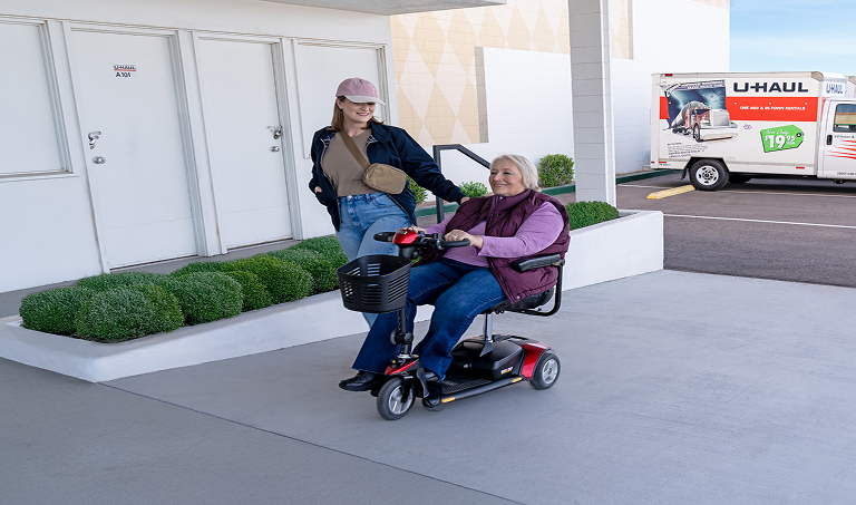 A woman in a motorized wheelchair, accompanied by a friend, using a wheelchair accessible ramp at a U-Haul Storage Facility