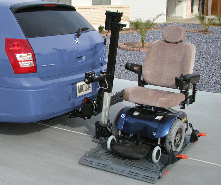 Motorized wheelchair secured on a hitch-mounted carrier attached to the back of a vehicle