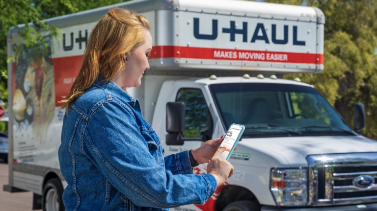 Woman using the U-Haul App in front of a U-Haul truck rental