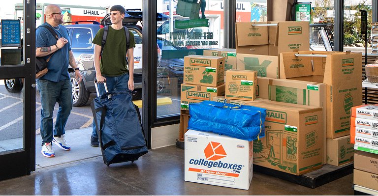 A college student unloading College boxes from a U-Haul Cargo van in front of a dorm