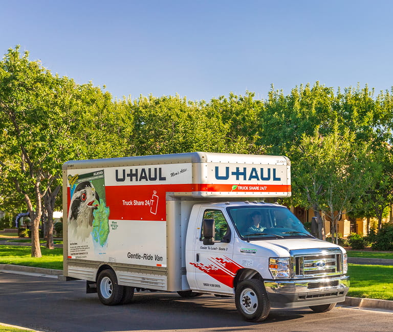 Un camion de déménagement U-Haul circulant sur une rue résidentielle bordée d’arbres.