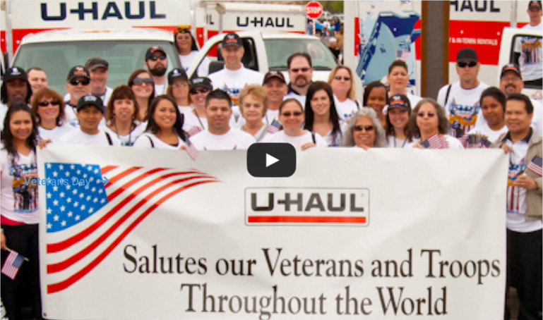 A group of U-Haul employees standing behind a banner saluting Veterans and Troops