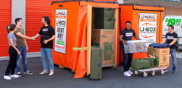 Military family standing next to a U-Box container with moving helpers loading their belongings