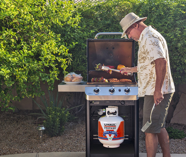 A propane grill with the top open, cooking meats and vegetables