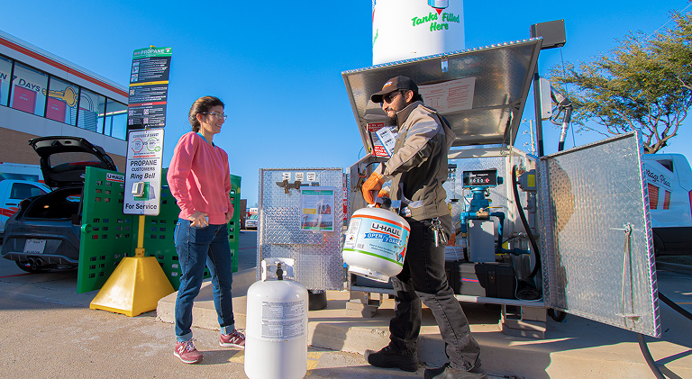 A woman watching a U-Haul employee fill a propane tank