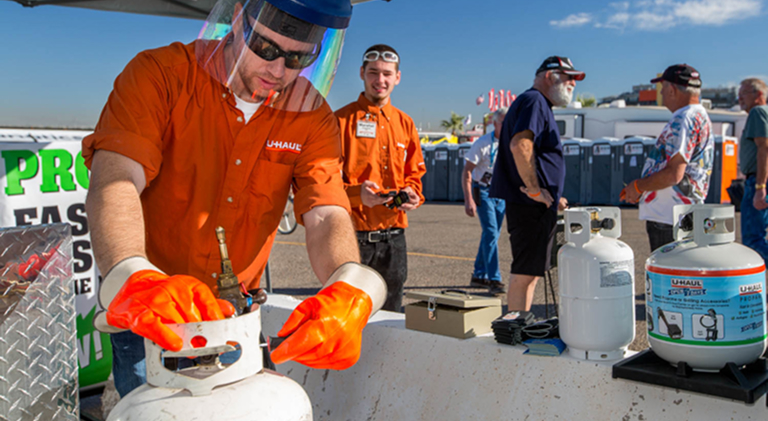 A U-Haul employee filling a propane tank as another employee and several customers watch