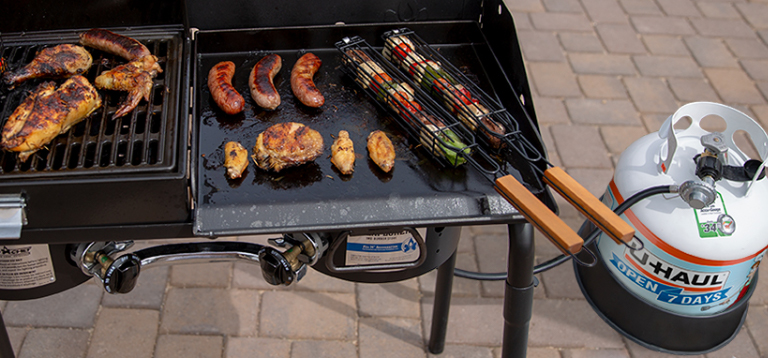 Propane grill with cooked meats and vegeatbles sitting on top