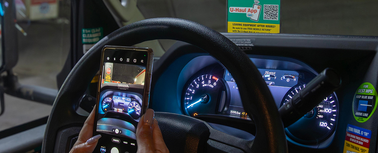 A woman sitting behind the wheel of a U-Haul Moving Truck, using a mobile device to return a rental