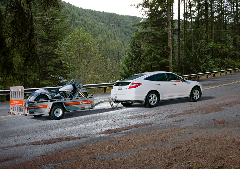 A car pulling a motorcycle in a U-Haul utility trailer