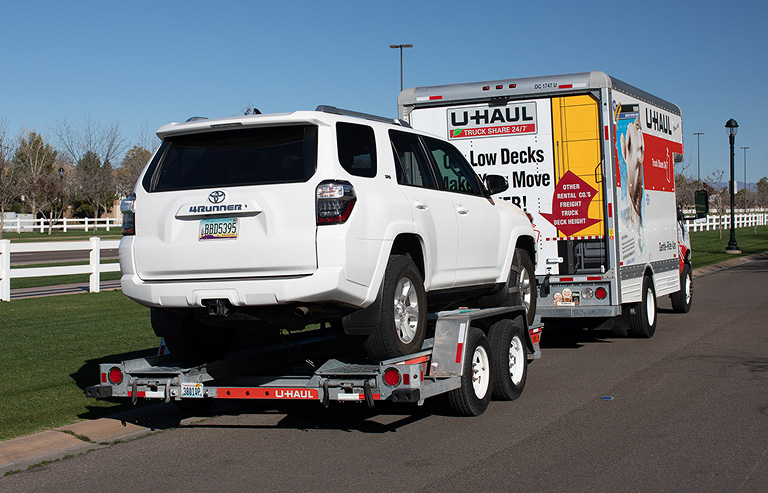 A U-Haul Truck towing a SUV secured to a U-Haul Auto Transporter