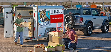 A couple unloading crates of produce from a U-Haul Cargo trailer