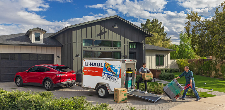 A couple loading moving boxes into a U-Haul cargo trailer