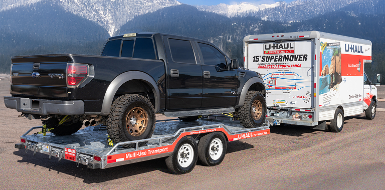 A U-Haul truck towing a pickup truck on a Toy Hauler trailer