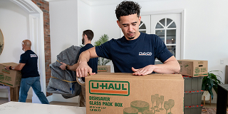 A group of moving helpers in a house with one focused on packing belongings into a moving box.