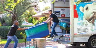 Two moving helpers loading a large aquarium into a U-Haul moving truck.