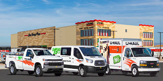 A line-up of a U-Haul pick up truck, cargo van, and small box truck parked in front of a U-Haul storage facility.