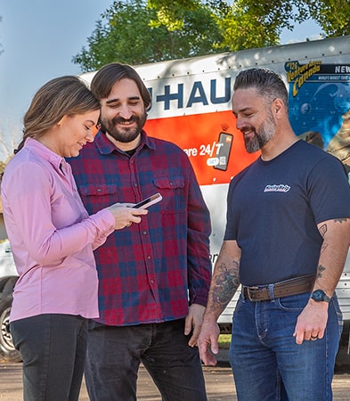 A couple standing with a moving helper using their phone to pay for the moving service.