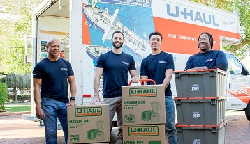 A group of Moving Helpers with loaded boxes standing in front of a U-Haul moving truck