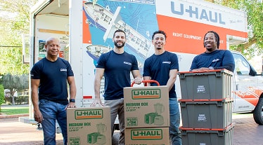A group of Moving Helpers with loaded boxes standing in front of a U-Haul moving truck