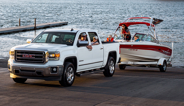 A family in a pick-up truck pulling a boat out of a lake and onto a trailer