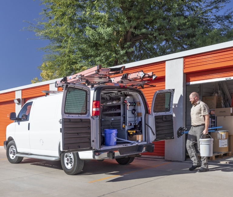 A man loading equipment into a work van from a business storage container