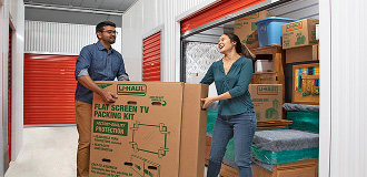 A couple in a climate-controlled U-Haul storage facility holding a large storage box while they load their storage unit